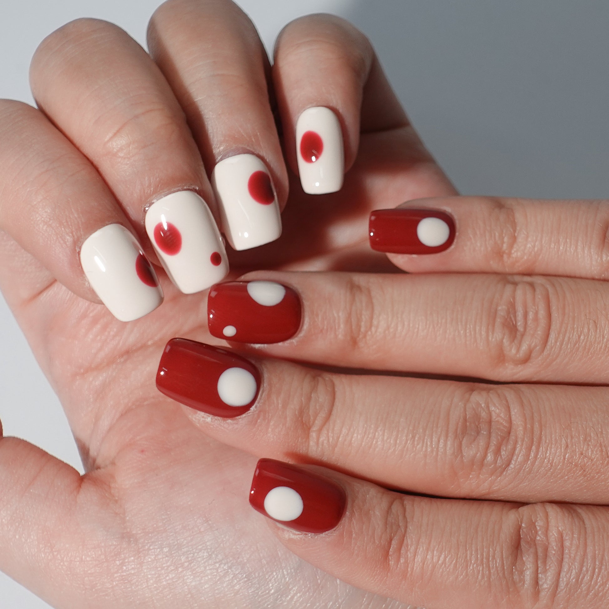 A set of press - on nails with a classic contrast of white and red, worn on a person's hand. The nails have a smooth finish with circular patterns, ideal for creating a bold and elegant appearance, suitable for both casual and formal events.