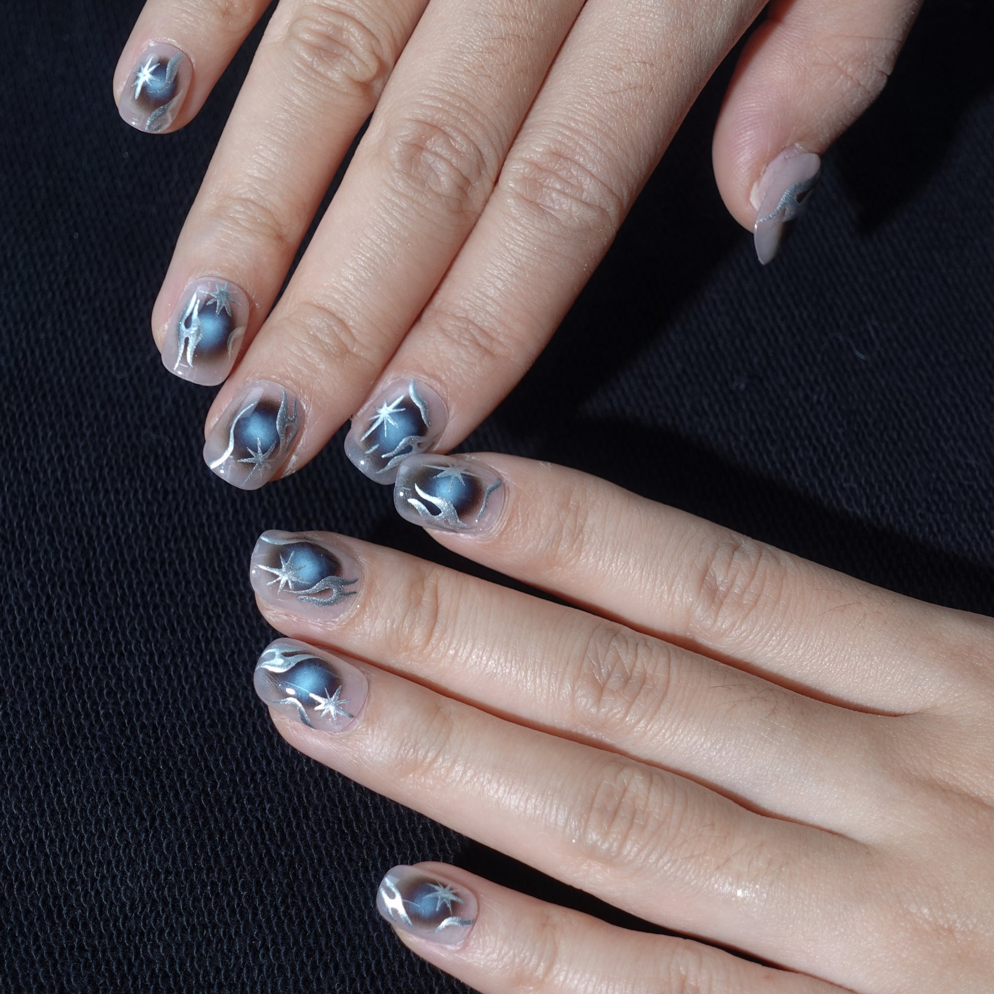 A set of handmade press - on nails with a dark - to - light gradient, featuring striking silver star - like designs. The nails have a bold, futuristic appearance, perfect for making a statement at night - time events or parties.