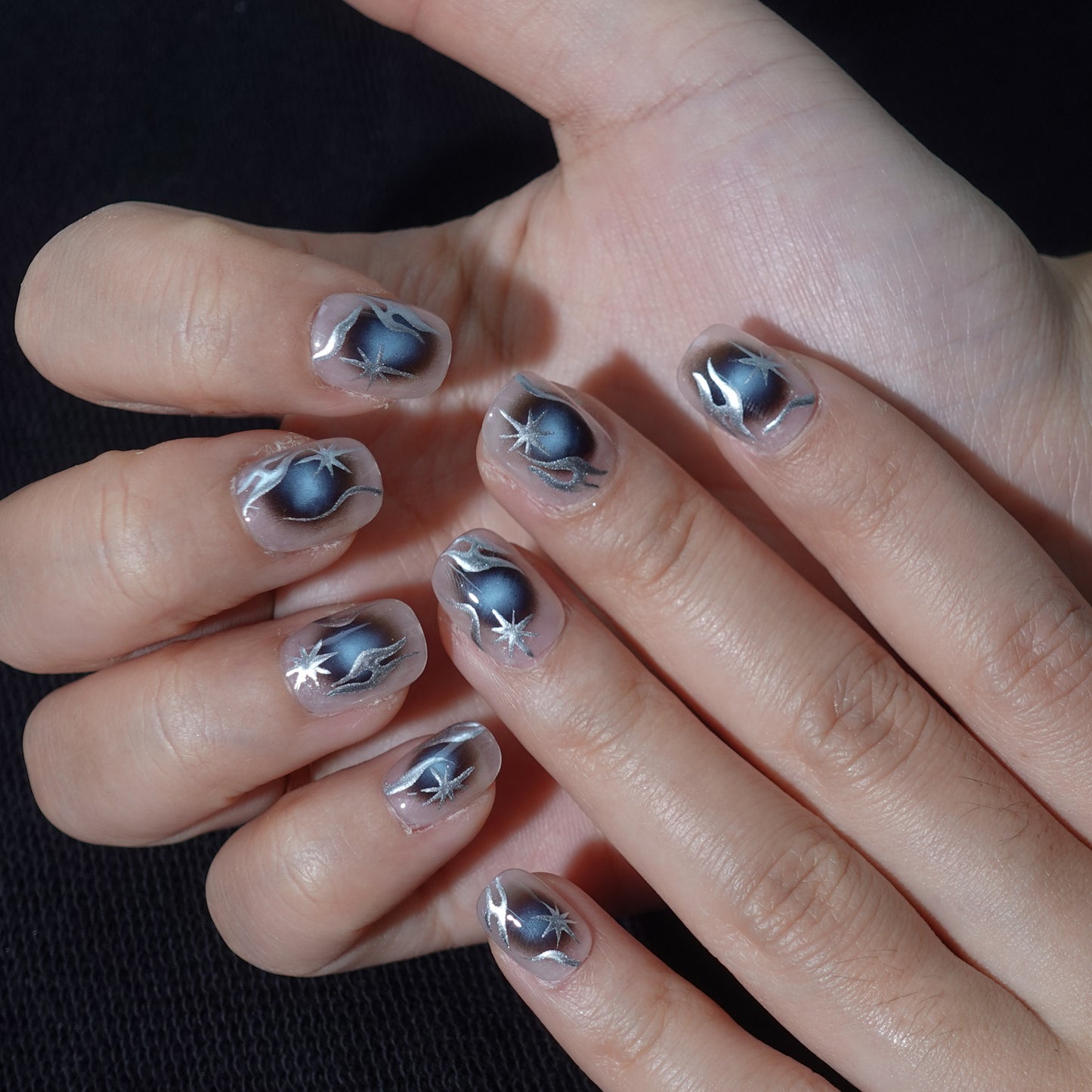 A set of handmade press - on nails with a dark - to - light gradient, featuring striking silver star - like designs. The nails have a bold, futuristic appearance, perfect for making a statement at night - time events or parties.