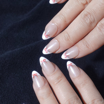 Minimalistic press-on nails featuring a nude base, white French tips, and red ribbon-inspired designs for a stylish and sophisticated look.