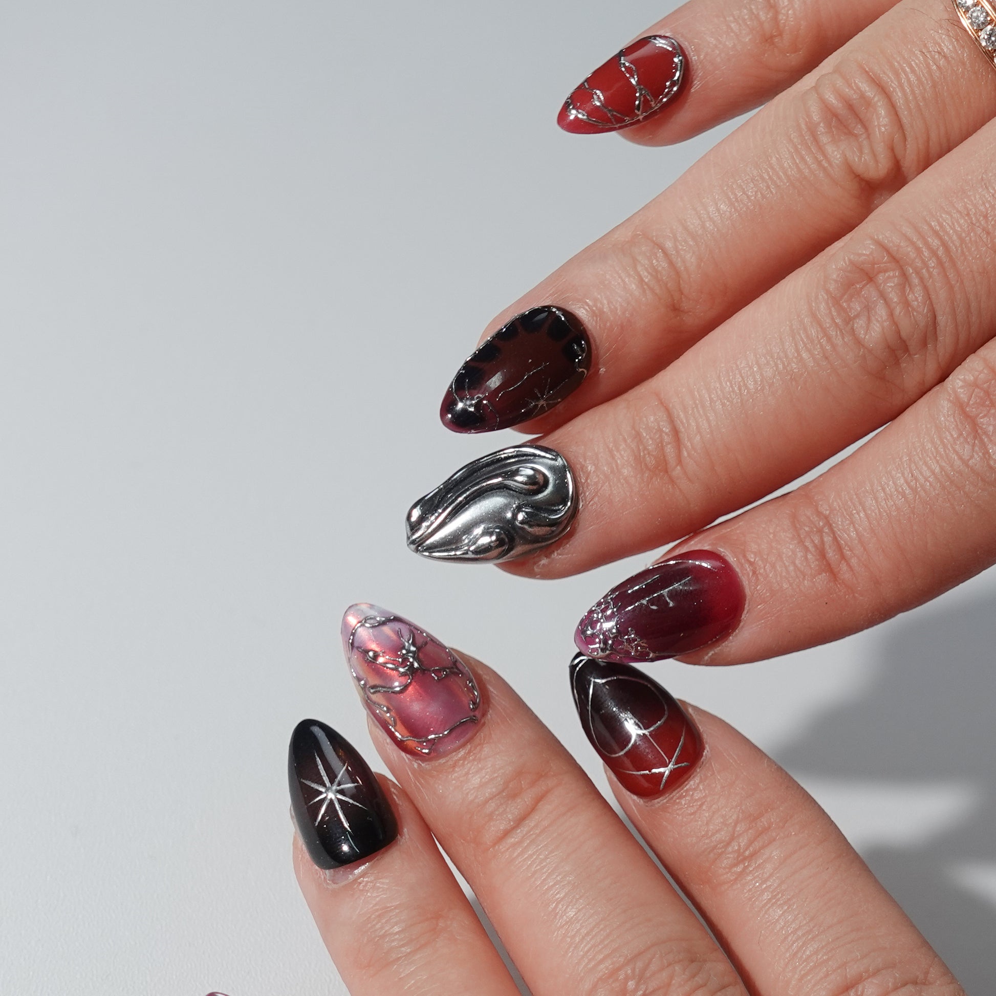 A set of handmade press-on nails featuring deep crimson and black tones, silver chrome details, radiant heart patterns, and a glossy finish. The perfect blend of passion and elegance for a bold, sophisticated look.