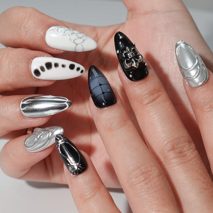 A luxurious set of press-on nails combining glossy black, crisp white, and shimmering silver tones. Featuring textures like metallic chrome, abstract patterns, and a fleur-de-lis embellishment, these nails are designed for bold, high-fashion statements.