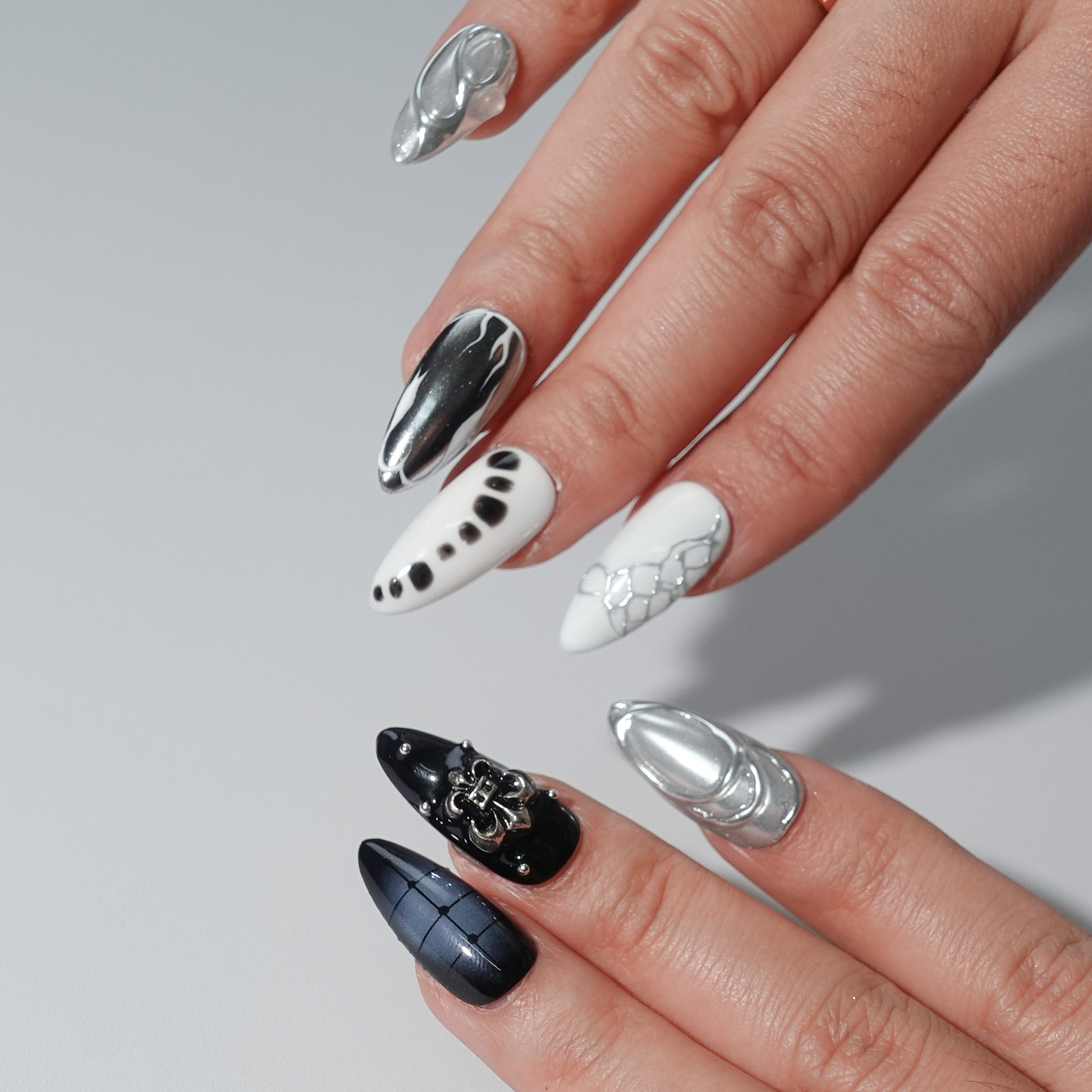 A luxurious set of press-on nails combining glossy black, crisp white, and shimmering silver tones. Featuring textures like metallic chrome, abstract patterns, and a fleur-de-lis embellishment, these nails are designed for bold, high-fashion statements.