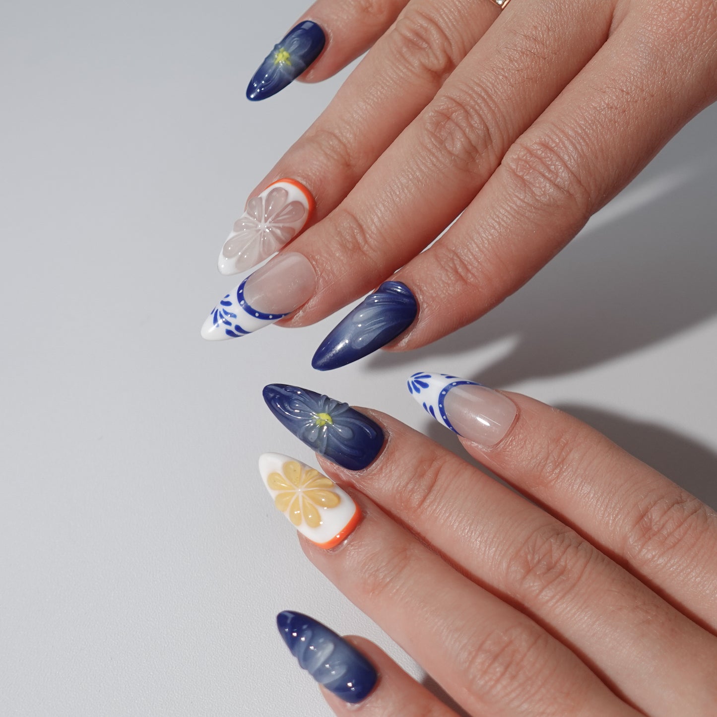 A lively set of handmade press-on nails featuring vibrant orange and pastel floral details, blended with soft blue gradients and intricate patterns. A cheerful and elegant design inspired by summer's energy and freshness.