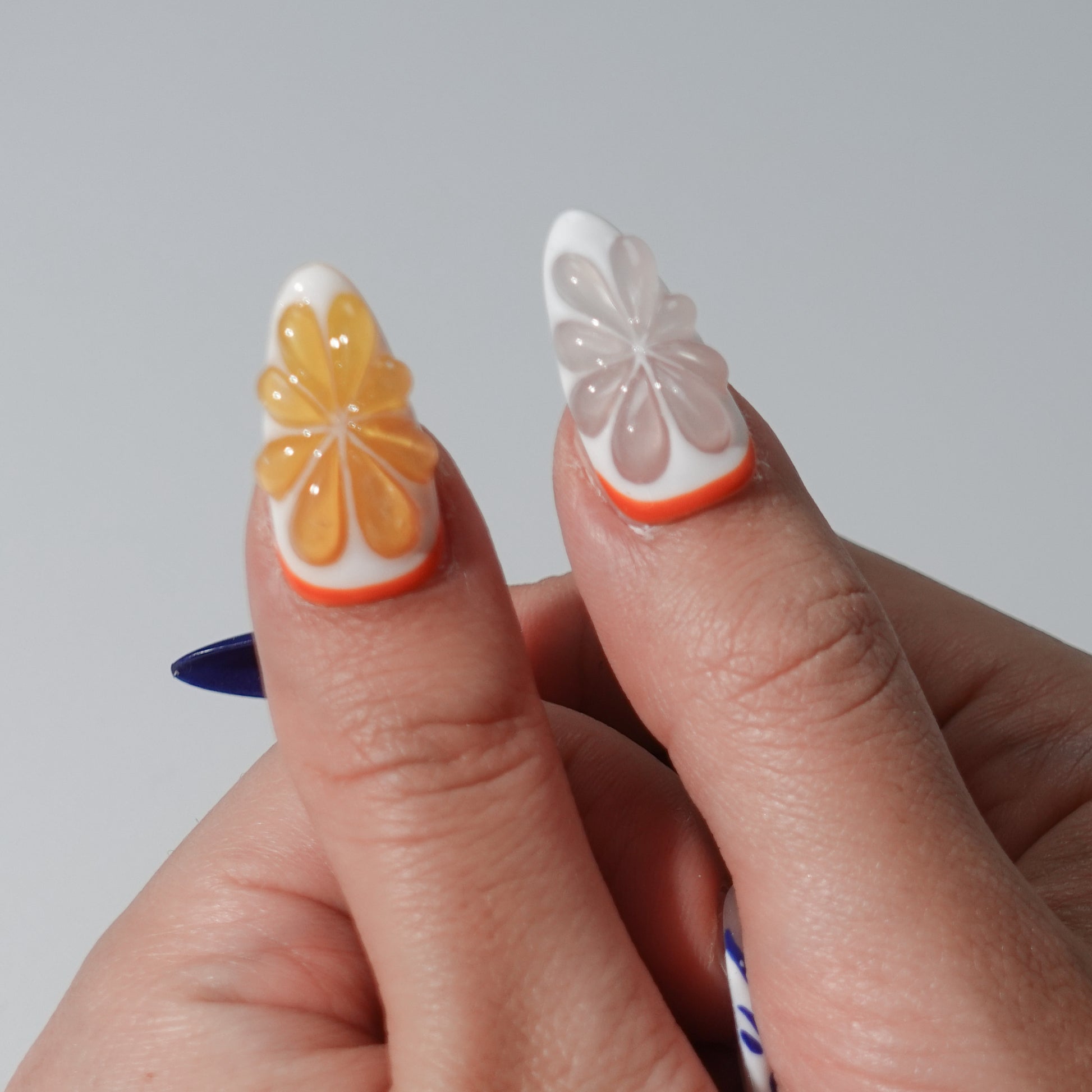 A lively set of handmade press-on nails featuring vibrant orange and pastel floral details, blended with soft blue gradients and intricate patterns. A cheerful and elegant design inspired by summer's energy and freshness.