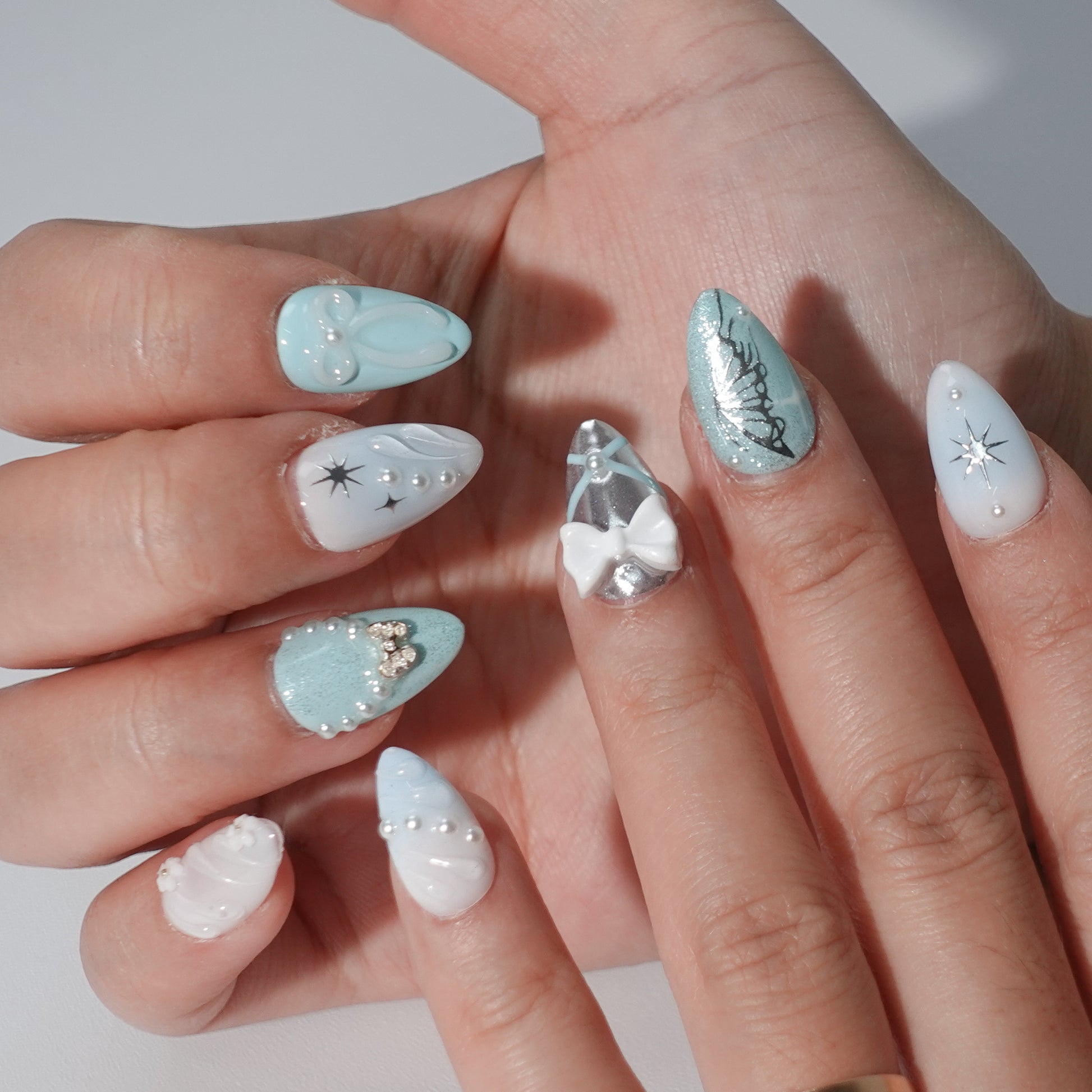 A sophisticated press-on nail design with a frosty blue color scheme, highlighted by snowflake-inspired star details, shimmering silver finishes, and delicate pearl and bow decorations. Perfect for capturing the charm of winter.