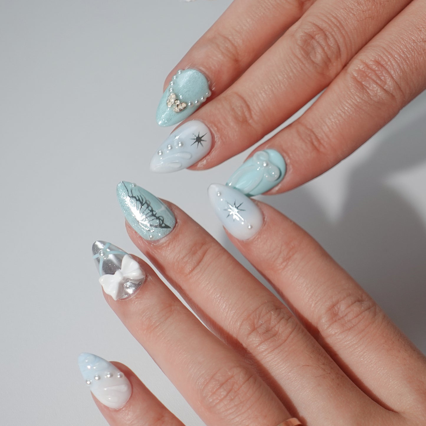 A sophisticated press-on nail design with a frosty blue color scheme, highlighted by snowflake-inspired star details, shimmering silver finishes, and delicate pearl and bow decorations. Perfect for capturing the charm of winter.