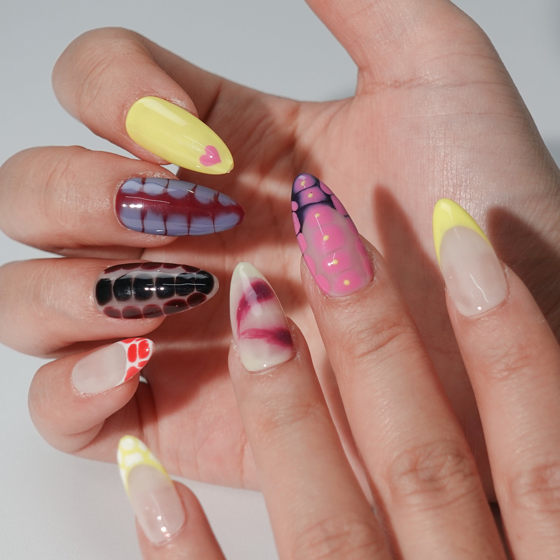 A press-on nail set featuring vibrant snake-skin-inspired patterns in pink, yellow, green, and maroon with glossy gradients, creating a bold and trendy design.