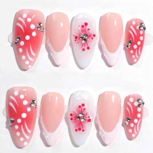 A handmade set of press-on nails showcasing pink gradients, intricate white petal-like designs, and 3D floral centers adorned with rhinestones, evoking the charm of blooming spring flowers under soft sunlight.