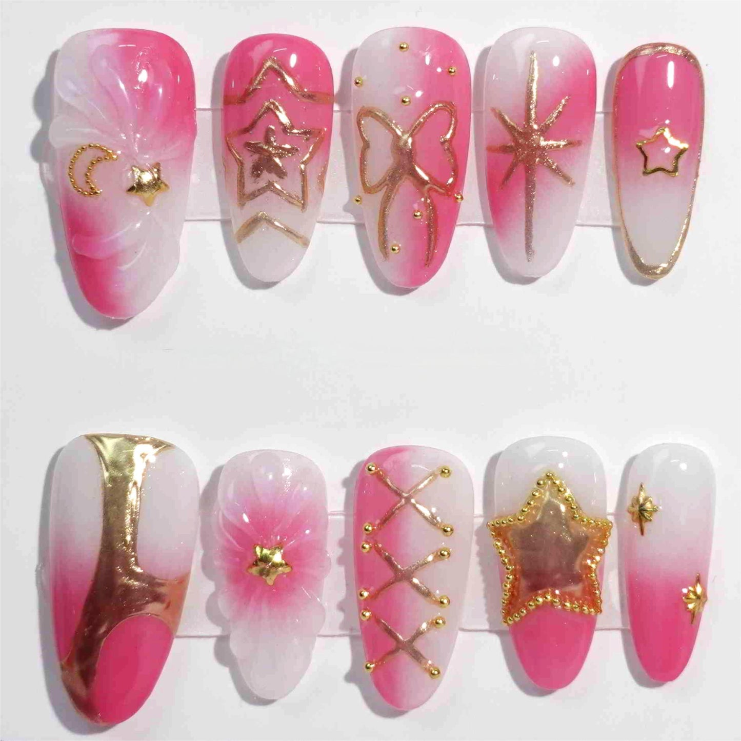 A stunning set of handmade press-on nails featuring celestial-themed designs, including golden stars, moons, and bows, with a graceful pink and white gradient.