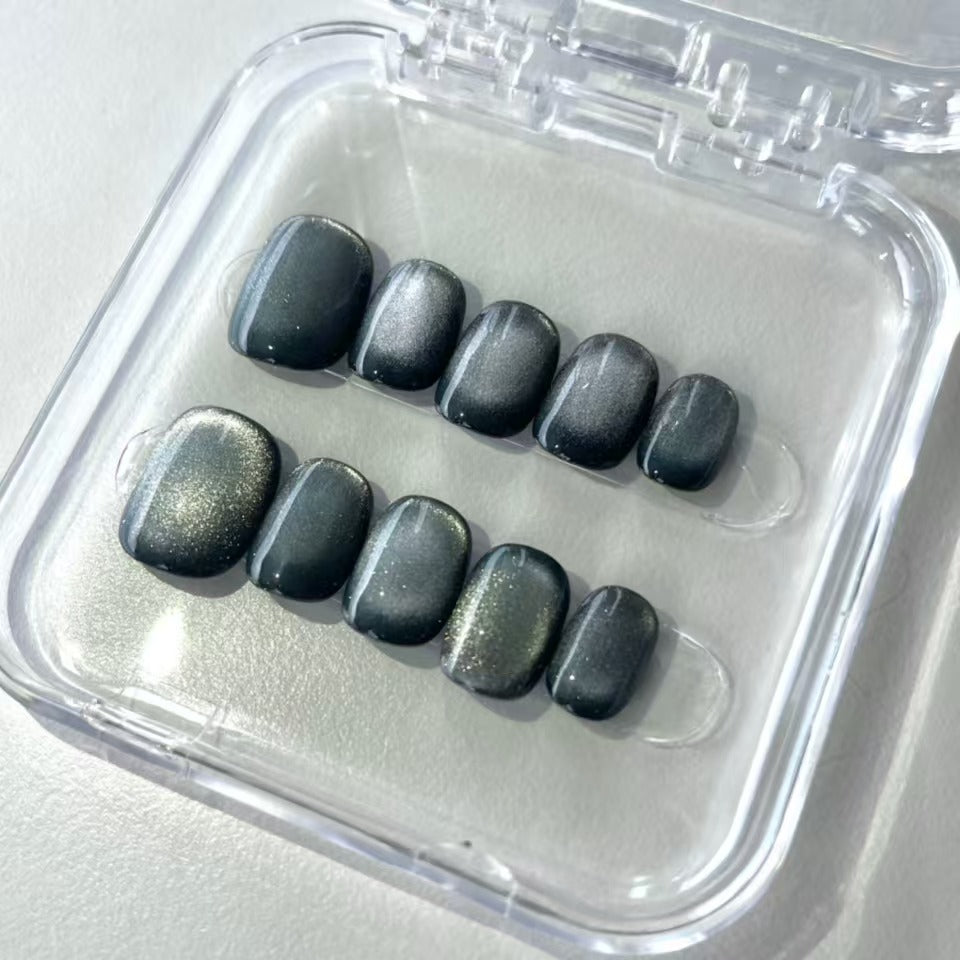 A set of gunmetal - colored glossy press - on nails worn on a person's hand. The nails have a smooth, shiny finish with a metallic appearance, giving them a bold and stylish look. The gunmetal hue adds an edgy flair, suitable for party or nightlife settings.