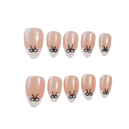 Press-on nails featuring a glimmering nude base with white tips and delicate black bow designs, perfect for a chic and elegant look.