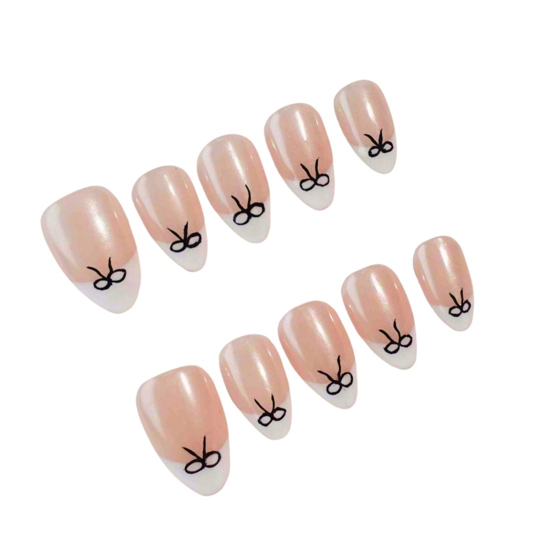 Press-on nails featuring a glimmering nude base with white tips and delicate black bow designs, perfect for a chic and elegant look.