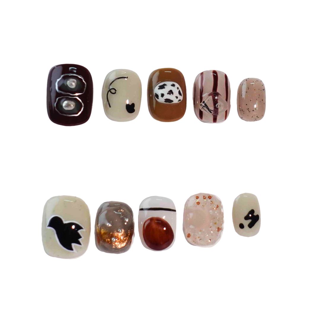 A stylish set of press-on nails blending warm earthy tones, abstract patterns, and creative details like cow prints, metallic accents, and playful animal shapes. Designed for those who love a blend of nature and artistry.