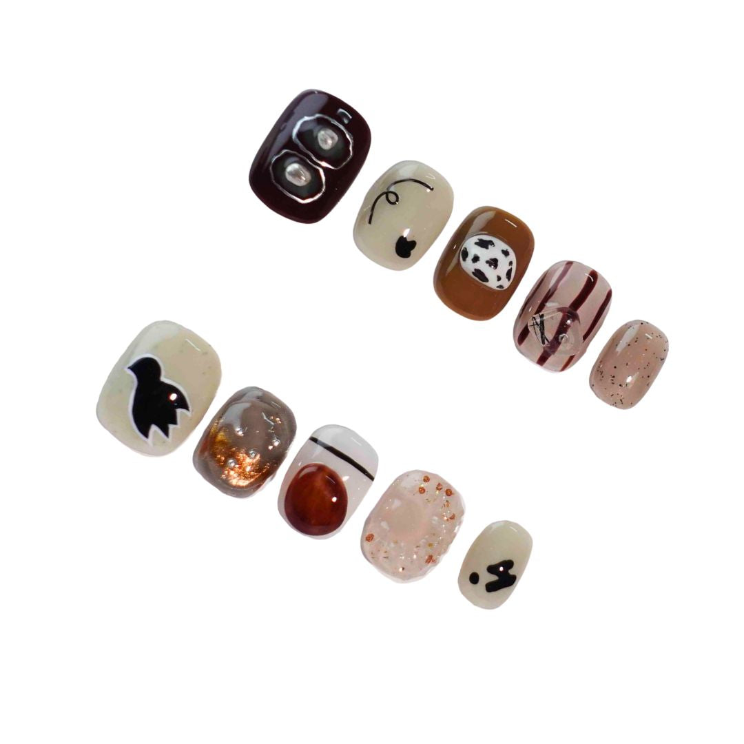 A stylish set of press-on nails blending warm earthy tones, abstract patterns, and creative details like cow prints, metallic accents, and playful animal shapes. Designed for those who love a blend of nature and artistry.