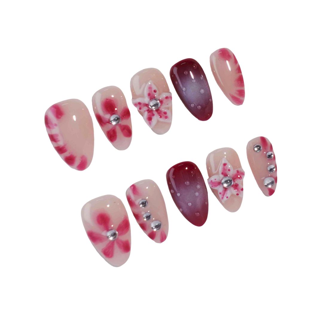 A set of press-on nails featuring a mix of soft pink and deep red tones, adorned with hand-painted floral designs and metallic silver embellishments. These nails create a romantic and chic aesthetic, ideal for evening events or celebrations.